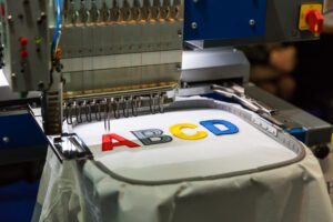 Professional sewing machine embroidery color letters. Textile fabric, nobody. Factory production, sew manufacturing, needlework technology logo tshirt corporate companies by gurgaon graphics printing