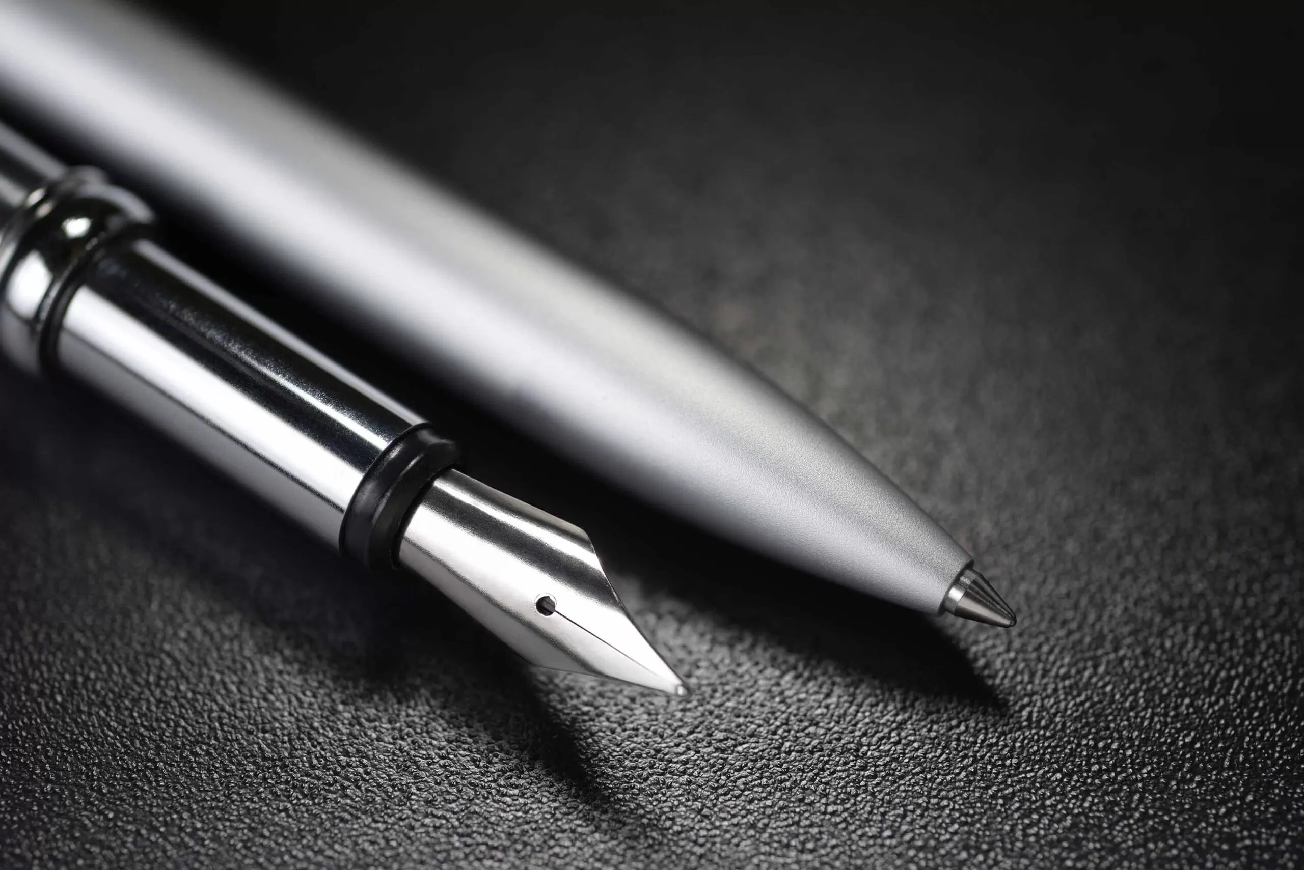 Modern ballpoint and antique fountain pen on dark black background